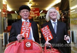 Sir Jimmy Savile poses with owner Warren Gold at Gold's Factory Outlet where he wore a suit to help promote...